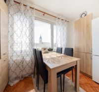 Ein Esstisch mit vier Stühlen in einer 3-Zimmer-Wohnung, Vorhänge mit geometrischem Muster.