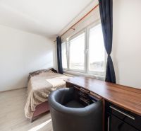 Ein Zimmer in einer 3-Zimmer-Wohnung mit Bett, Tisch und Fenstern mit dunklen Vorhängen.
