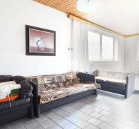 Ein Zimmer in einem Einfamilienhaus mit einem Sofa, einem Bild an der Wand und großen Fenstern.
