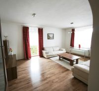 Wohnzimmer eines Einfamilienhauses mit Holzboden, weißen Möbeln und roten Vorhängen.