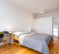 Schlafzimmer in einer 2-Zimmer-Wohnung mit Bett, Schreibtisch und Boden mit Holzdekor.