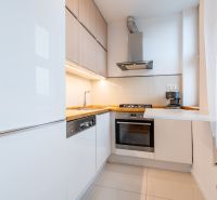 Helle Küche in einer Zweizimmerwohnung mit weißen Schränken und Holzelementen.