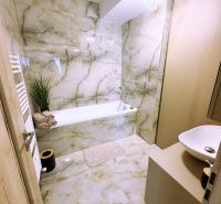 Badezimmer mit Badewanne, Kronleuchter und Marmorverkleidung in einer 2-Zimmer-Wohnung.