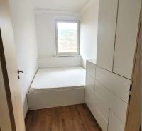 Ein schmales Zimmer mit einem Bett und Einbauschränken, Boden mit Holzdekor.