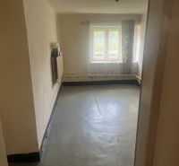 Ein Zimmer in einem Einfamilienhaus mit Betonboden und einem Fenster mit einfallendem Licht.
