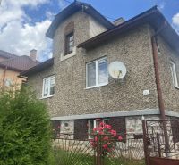 Ein Einfamilienhaus in Rudná mit einer strukturierten Fassade, einem grünen Zaun und Blumen im Garten.