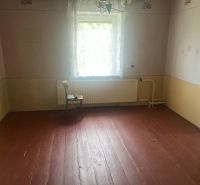Ein Zimmer in einem Einfamilienhaus mit Holzboden, Wände in Pastellfarben, Fenster mit weißem Vorhang.
