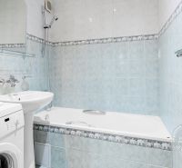 Badezimmer mit Badewanne, Waschmaschine und Waschbecken in einer 2-Zimmer-Wohnung mit hellblauen Fliesen.