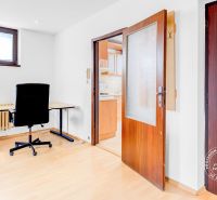 Innenraum einer 2-Zimmer-Wohnung mit einem Bürobereich, einem Regal und einer Tür zur Küche.