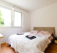 Schlafzimmer in einer 2-Zimmer-Wohnung mit Fenster, Bett und Boden in Holzoptik.