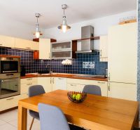 Küche in einer 2-Zimmer-Wohnung mit Holztisch, blauen Fliesen und hellen Schränken.
