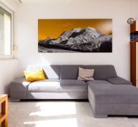 Wohnzimmer in einer 2-Zimmer-Wohnung, graues Sofa, Bild von Bergen, helle Wände.