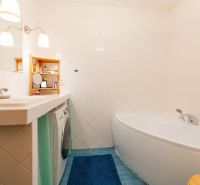 Badezimmer mit Badewanne, Waschmaschine, blauem Teppich und weißen Fliesen in einer 2-Zimmer-Wohnung.