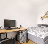 Schlafzimmer in einer 2-Zimmer-Wohnung mit Bett, Tisch und Boden in Holzoptik.