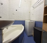 Badezimmer in einer Einzimmerwohnung mit Badewanne und Waschmaschine, gefliest mit weißen und blauen Fliesen.