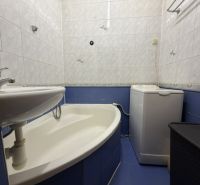 Badezimmer in einer Einzimmerwohnung mit Dusche, Waschbecken, Waschmaschine und blauen Fliesen.