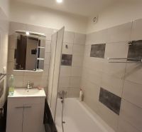 Badezimmer mit Badewanne und Waschbecken in einer Zweizimmerwohnung, gefliest mit hellen Fliesen.