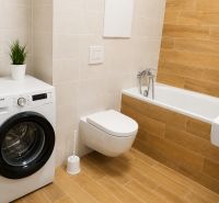 Badezimmer mit Toilette, Badewanne, Waschmaschine und Holzboden in einer Einzimmerwohnung.