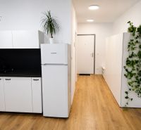 Küche in einer Einzimmerwohnung mit schwarzem Spülbecken, weißen Schränken und einem Boden in Holzoptik.