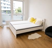Einzimmerwohnung mit Bett, Sessel, Holzboden und Balkontüren.