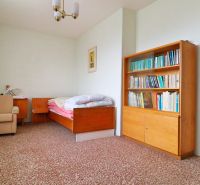 Ein Zimmer in einem Einfamilienhaus mit einem Stuhl, einem Bett, einem Regal und einem bunten Teppich.