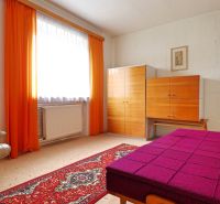 Ein Zimmer in einem Einfamilienhaus mit einem hellen Sessel, Möbeln und auffälligen orangefarbenen Vorhängen.