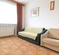 Wohnzimmer mit Sofa, Sessel, Bildern an der Wand, Holzboden.