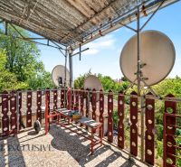 Der Balkon eines Einfamilienhauses in Bodza mit Satellitenschüsseln und Grün im Hintergrund.