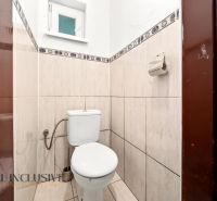 Kleines Badezimmer mit Toilette, gefliest mit hellen Fliesen, mit Fenster und Papierhalter.