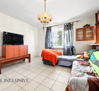 Wohnzimmer mit Fernseher, Sofa und Schrank in einem Einfamilienhaus, Licht durch Vorhänge.