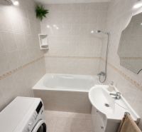 Badezimmer mit Badewanne, Waschbecken und Waschmaschine in einer 3-Zimmer-Wohnung, helle Fliesen.