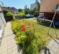 Blumenbeete an der Straße in Krupina, neben einer 2-Zimmer-Wohnung, Auto unter einem Unterstand geparkt.
