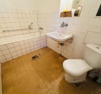 Badezimmer in einer 2-Zimmer-Wohnung mit Badewanne, Waschbecken und Toilette, gefliest mit weißen Fliesen.