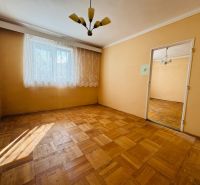 Ein Zimmer in einer 2-Zimmer-Wohnung mit einem Boden in Holzoptik und Vorhängen am Fenster.