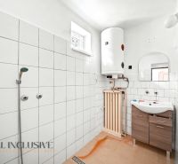 Badezimmer im Einfamilienhaus mit Fliesen, Dusche, Boiler und Waschbecken mit Holzmaske.