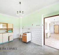 Eine Küche in einem Einfamilienhaus mit einer einfachen Küchenzeile, weißen Fliesen und einem grauen Boden.