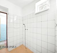Ein Badezimmer in einem Einfamilienhaus mit weißen Fliesen und einer einfachen Dusche.