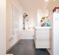 Badezimmer in einer 3-Zimmer-Wohnung mit dunklem Boden und hellen Möbeln.