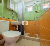 Ein Badezimmer in einem Einfamilienhaus mit orange-grünen Fliesen und einer Duschkabine.
