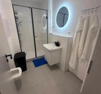 Badezimmer mit rundem Spiegel, Duschkabine und Waschbecken in einer Zweizimmerwohnung.