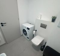 Badezimmer mit Waschmaschine, Toilette und beigefarbenen Fliesen in einer 2-Zimmer-Wohnung.