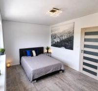 Schlafzimmer in einem Einfamilienhaus mit großem Fenster, Bett und Boden mit Holzdekor.