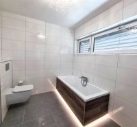 Badezimmer in einem Einfamilienhaus mit einer Badewanne in Holzoptik und einem großen Fenster.