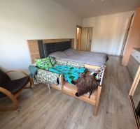 Schlafzimmer in einer 3-Zimmer-Wohnung mit Bett, Sessel und Boden in Holzoptik.