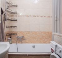 Badezimmer mit Badewanne und Waschmaschine in einer 2-Zimmer-Wohnung. Fliesen mit beigem Dekor.