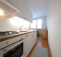 Küche in einer 2-Zimmer-Wohnung mit weißen Schränken und einem Boden in Holzoptik.