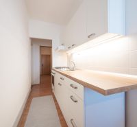 Eine schmale Küche mit weißen Schränken, Fliesenrückwand und Holzboden in einer Zweizimmerwohnung.