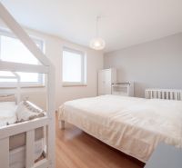 Helles Schlafzimmer in einer 2-Zimmer-Wohnung mit Bett, Kinderbett und Boden in Holzoptik.