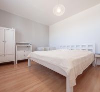 Schlafzimmer in einer 2-Zimmer-Wohnung mit Holzdekorboden, hellen Möbeln und einer Lampe.