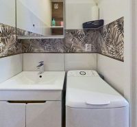 Badezimmer in einer Ferienwohnung mit Waschmaschine und gemusterten Fliesen an den Wänden.